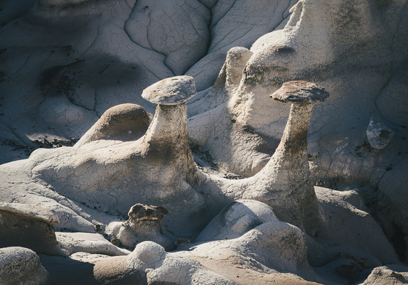 A striking landscape of unique rock formations, resembling mushroom shapes, with textured surfaces and a weathered appearance, set against a backdrop of rugged terrain.