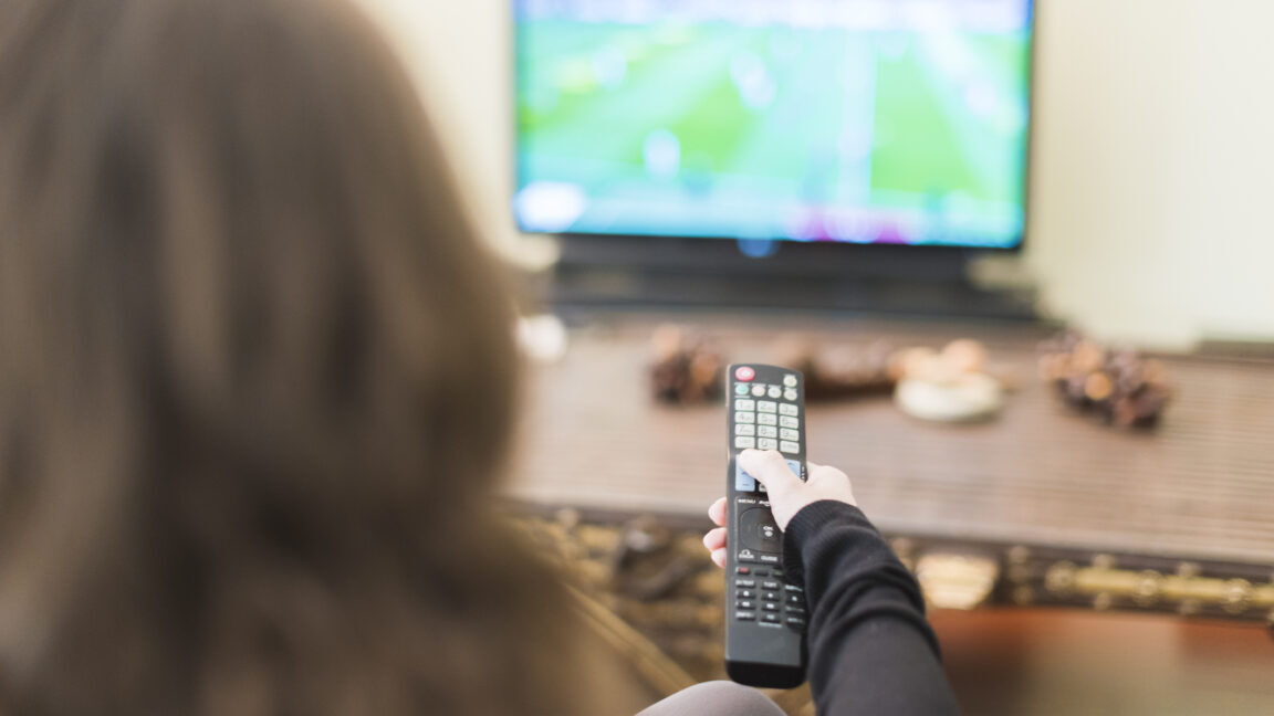 A woman changing television channels with the remote control.