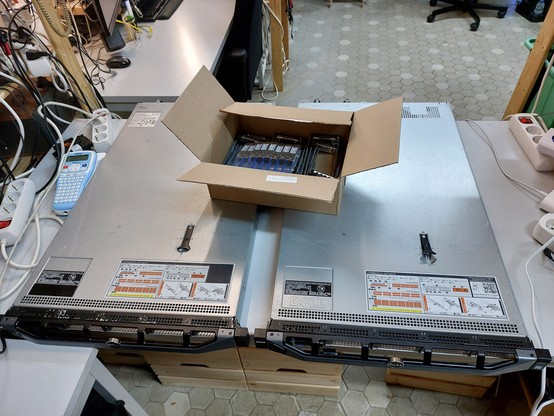 Auf einem Tisch liegen zwei Server. Auf den Servern steht ein Karton mit SFP Modulen.