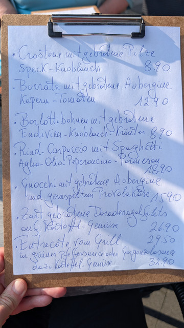 Die mit blauem Kuli auf weißem Papier handgeschriebene Speisekarte. 