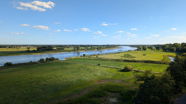 Auf beiden Bildern sind grüne Elbwiesen. Mittig der Fluss. Unter blauem Himmel mit wenigen weißen Wolken. 