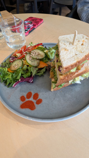 Ein veganes Sandwich mit Salat auf einem Teller, auf dem mit rotem Paprikapulver eine Katzenpfote geformt wurde. 