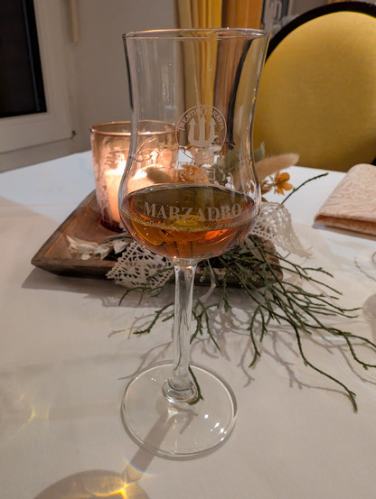 Das Grappaglas vor einer Kerze und Blumenschmuck. Die Farbe des Getränks ist braun. 