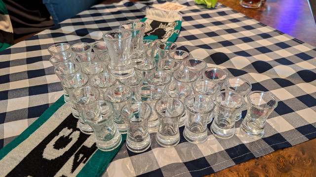 Eine über die Mitte des Tisches im Restaurant reichende Raute aus geleerten Ouzo Gläsern. 
