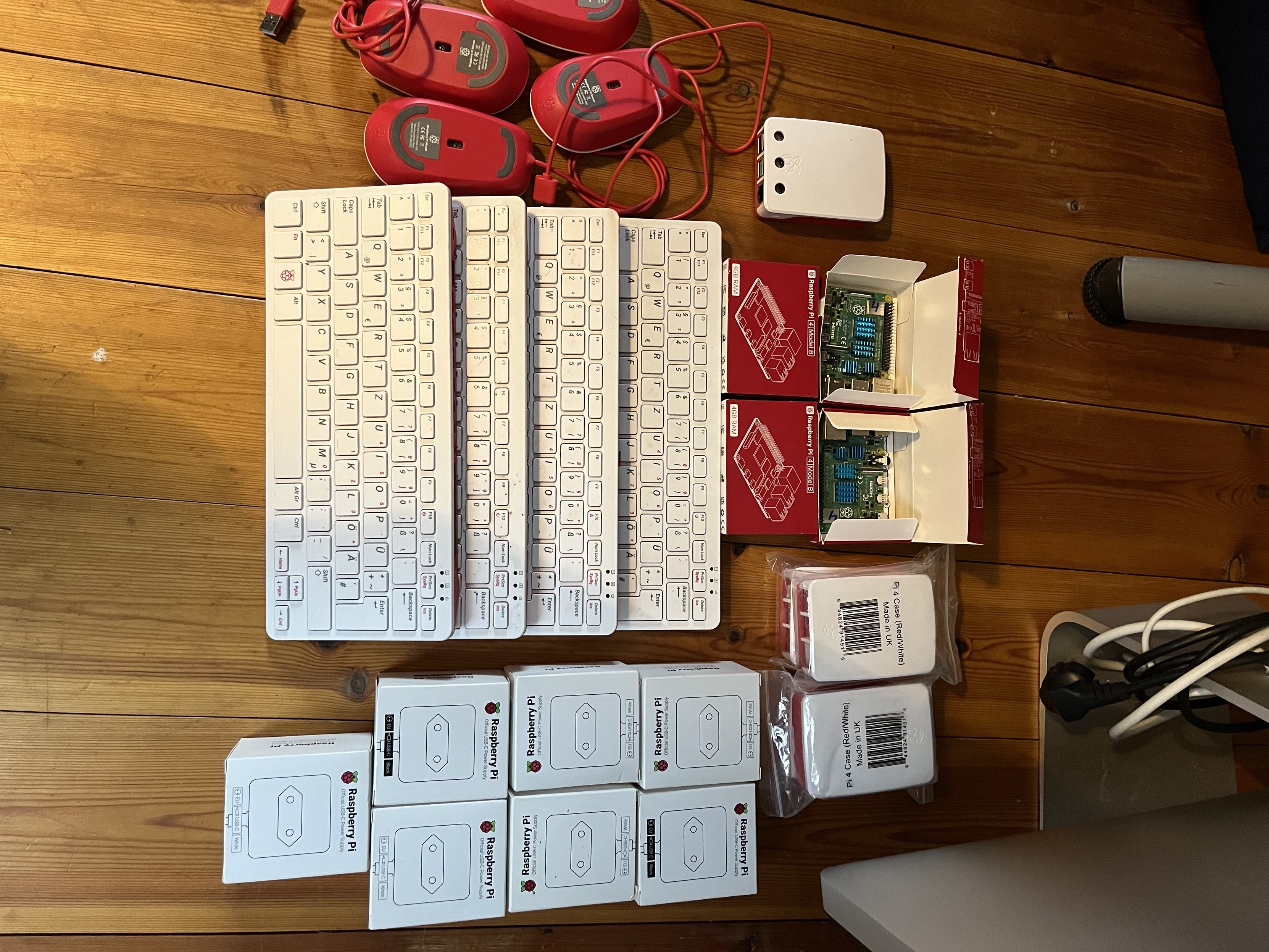 Photo von mehreren Raspberry 4 und 400 auf einem Holzboden liegend.
Dazu 7 Netzteile und 4 Mäuse.