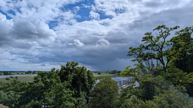 Bäume im Vordergrund.
Mittig und links ist Wasser des Tanger und der Elbe zu erkennen.
Am Horizont sehr dunkle Unwetter-Wolken.