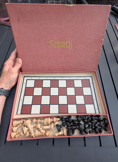 Der aufgeklappte Karton mit dem Spielfeld und den Holzfiguren in einem Fach davor liegt auf unserem Gartentisch. 